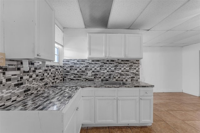 kitchen with decorative backsplash, a sink, baseboards, white cabinets, and light tile patterned flooring