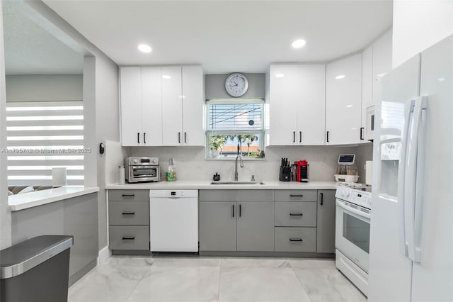 kitchen with gray cabinetry, light countertops, a sink, marble finish floor, and white appliances
