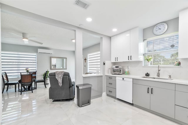 kitchen featuring white dishwasher, a sink, light countertops, a wall unit AC, and visible vents