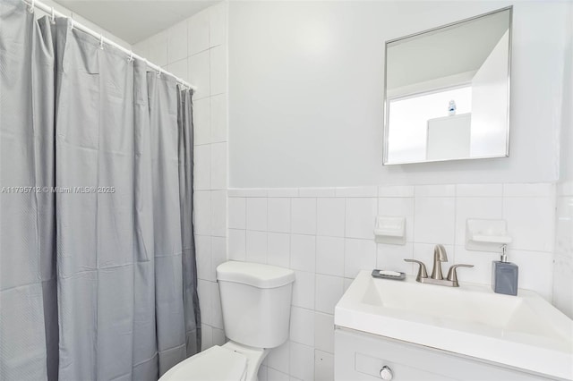 bathroom featuring vanity, toilet, tile walls, a shower with shower curtain, and a wainscoted wall