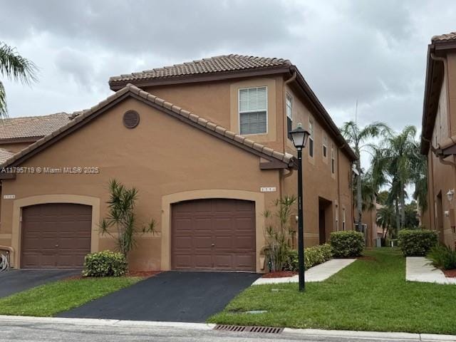 mediterranean / spanish-style home featuring a garage, a front lawn, aphalt driveway, stucco siding, and a tile roof
