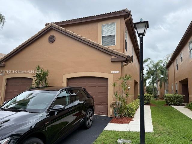 view of front of property with a front lawn, stucco siding, an attached garage, and a tile roof