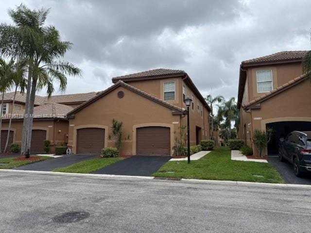 view of front of property featuring a tiled roof, aphalt driveway, a front lawn, and stucco siding