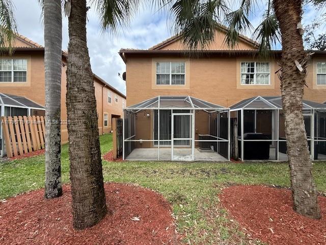 rear view of house with a lanai, fence, a yard, a patio, and stucco siding