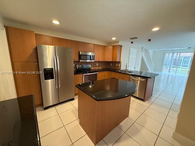 kitchen with dark countertops, a sink, stainless steel appliances, a peninsula, and light tile patterned floors