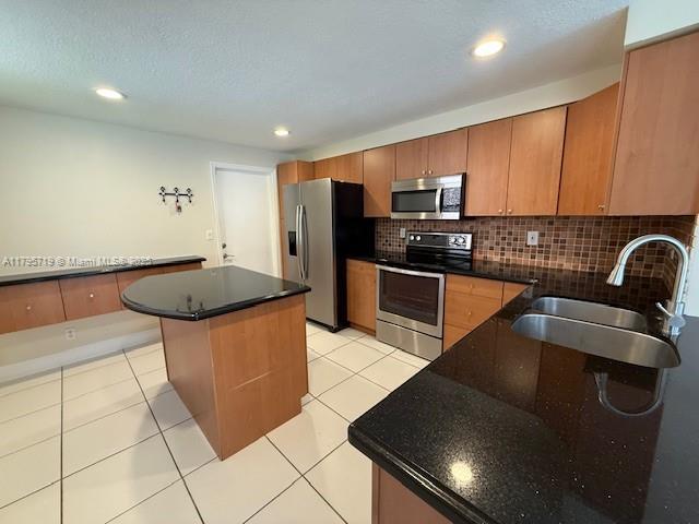 kitchen with appliances with stainless steel finishes, a sink, decorative backsplash, light tile patterned floors, and a kitchen island