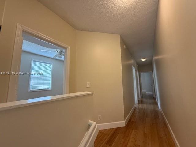 hall with baseboards, a textured ceiling, and wood finished floors