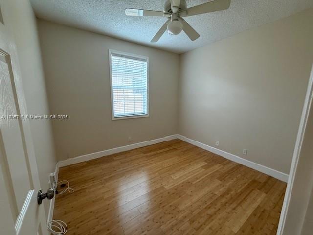 spare room featuring baseboards, ceiling fan, light wood-type flooring, and a textured ceiling