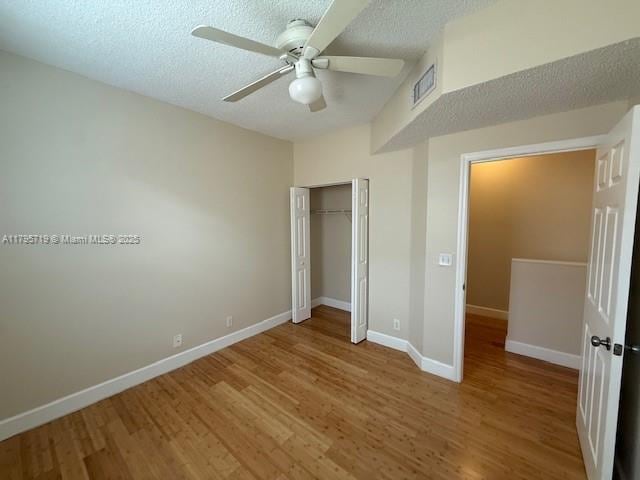 unfurnished bedroom featuring a textured ceiling, visible vents, wood finished floors, baseboards, and a closet