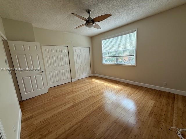 unfurnished bedroom with light wood-style floors, multiple closets, baseboards, and a textured ceiling