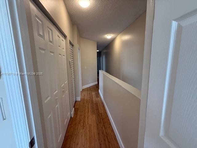 hallway featuring baseboards, a textured ceiling, and wood finished floors