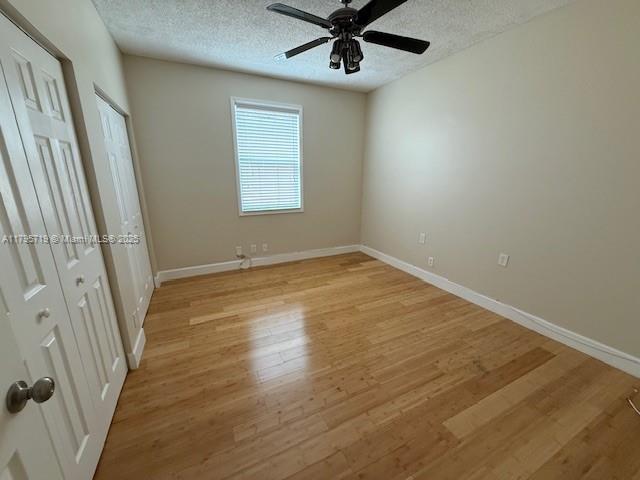 unfurnished bedroom featuring light wood-style floors, baseboards, a ceiling fan, and a textured ceiling