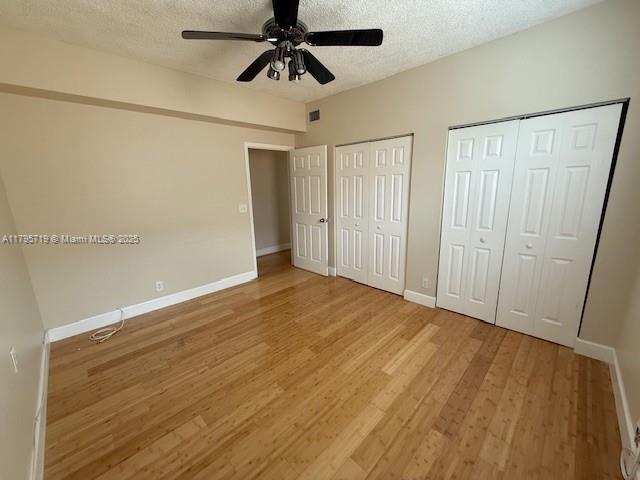 unfurnished bedroom with two closets, a textured ceiling, baseboards, and light wood-type flooring