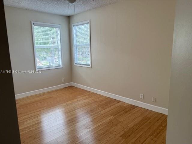 spare room featuring light wood-style floors, baseboards, ceiling fan, and a textured ceiling