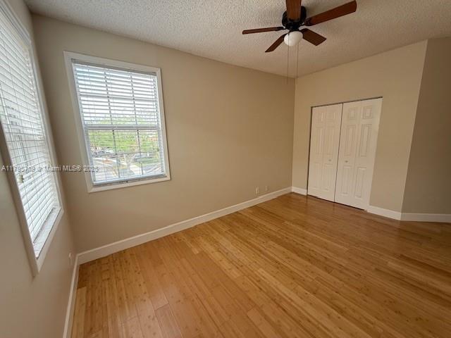 unfurnished bedroom featuring a textured ceiling, multiple windows, baseboards, and light wood finished floors