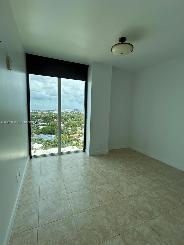 empty room featuring tile patterned flooring, baseboards, and expansive windows