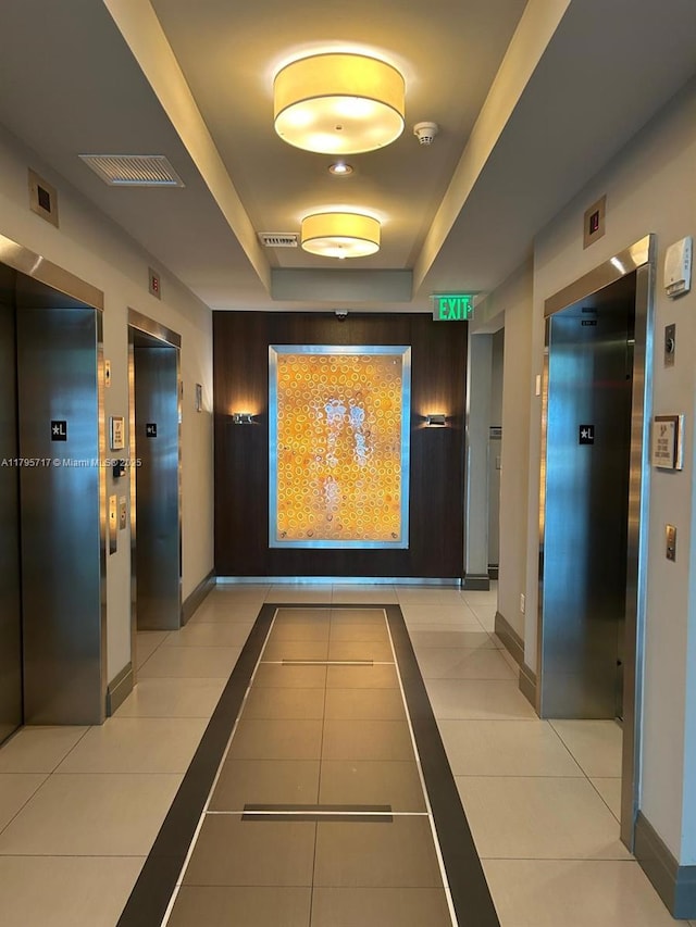 hallway featuring light tile patterned floors, elevator, baseboards, and a raised ceiling