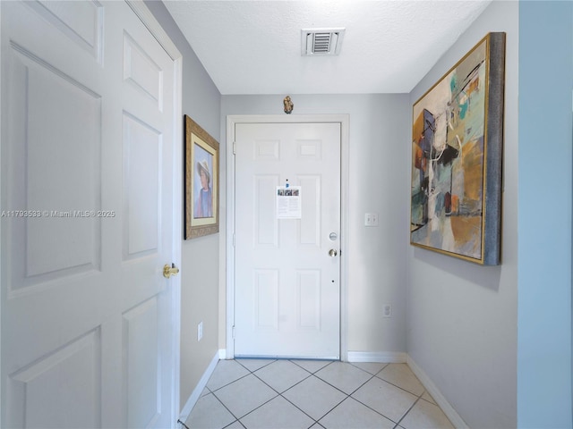 doorway featuring a textured ceiling, baseboards, visible vents, and light tile patterned floors
