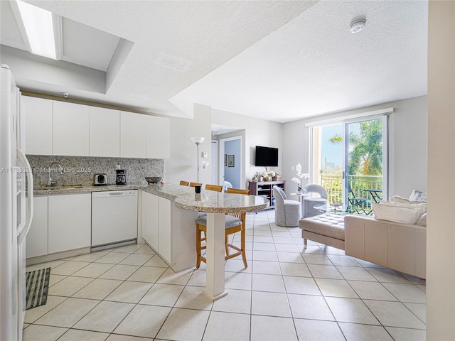 kitchen with a sink, white appliances, white cabinetry, open floor plan, and backsplash