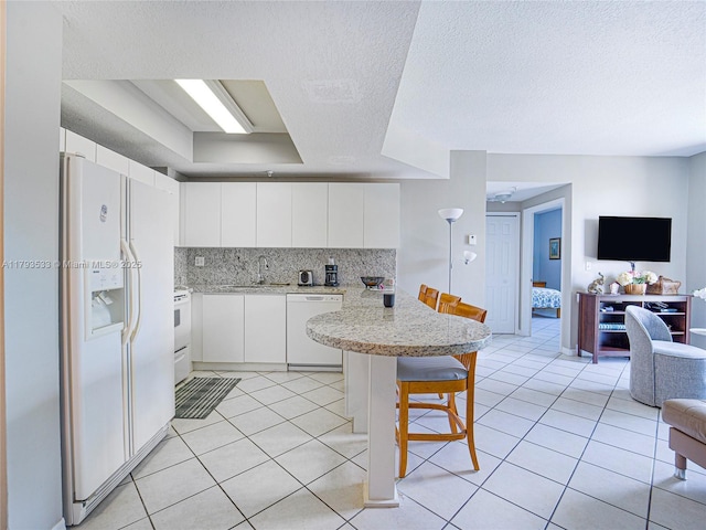 kitchen with a breakfast bar area, a sink, open floor plan, white appliances, and white cabinetry