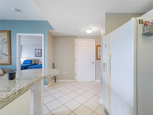 kitchen with light tile patterned floors, baseboards, white refrigerator with ice dispenser, and a textured ceiling