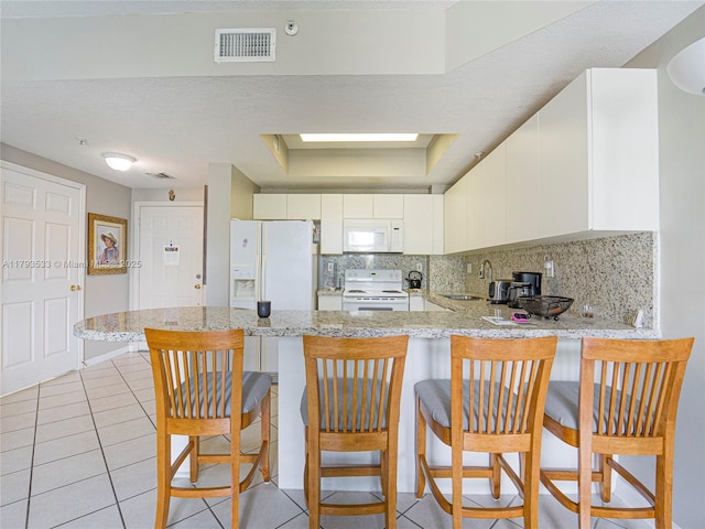 kitchen featuring a peninsula, white appliances, light tile patterned flooring, and visible vents