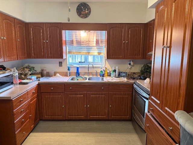 kitchen with a sink, stainless steel electric range, brown cabinets, and light countertops