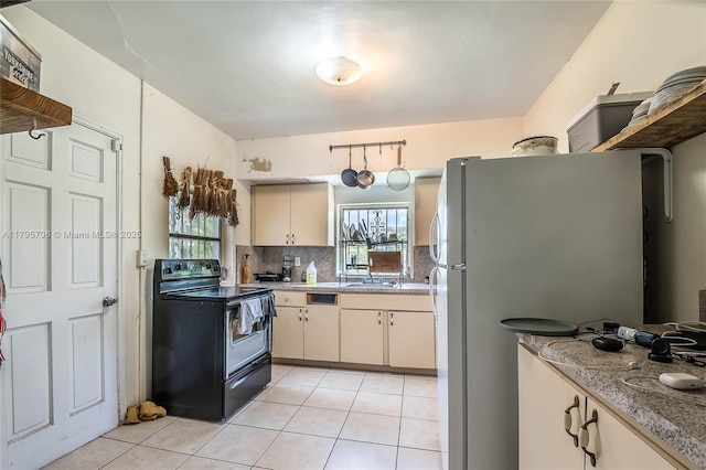 kitchen featuring freestanding refrigerator, light tile patterned flooring, a healthy amount of sunlight, and black / electric stove