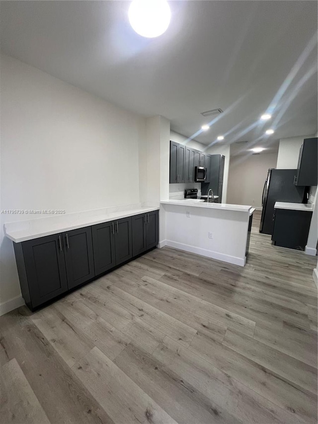 kitchen with light countertops, a peninsula, stainless steel microwave, and light wood-style floors