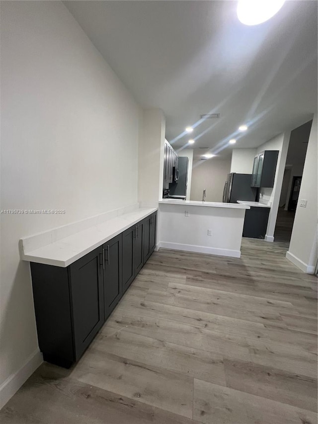 interior space with freestanding refrigerator, a peninsula, baseboards, and lofted ceiling