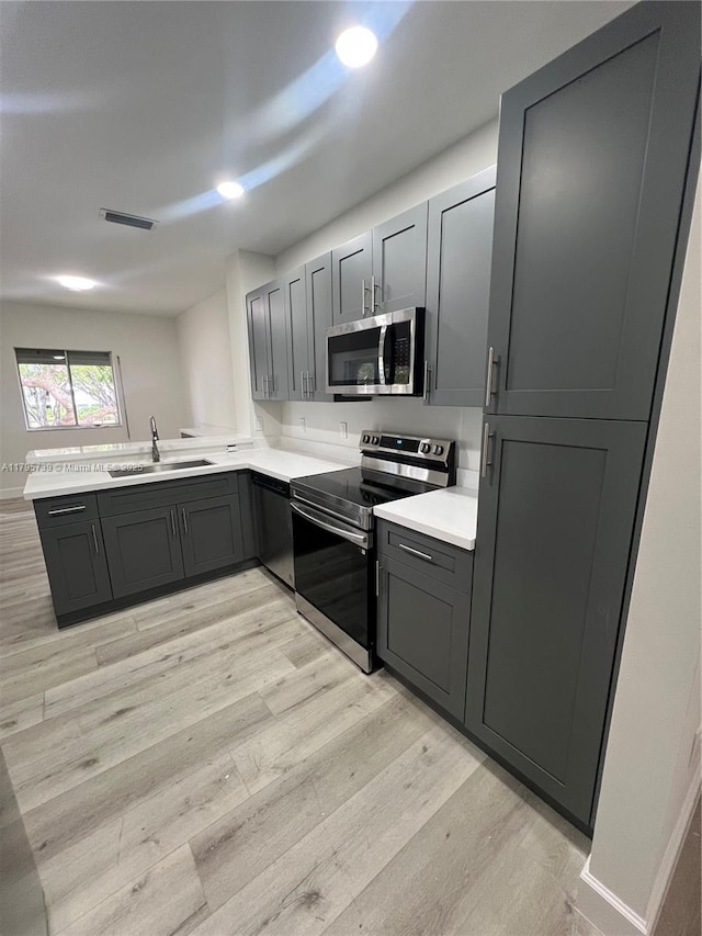 kitchen featuring light countertops, gray cabinets, a sink, light wood finished floors, and stainless steel appliances