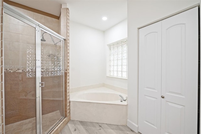 full bathroom featuring a bath, a shower stall, and wood finished floors
