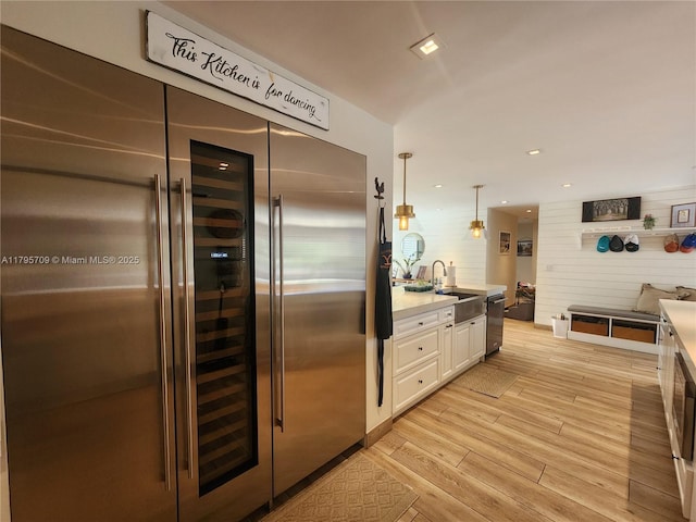 kitchen with white cabinets, a sink, light wood-style floors, light countertops, and built in refrigerator