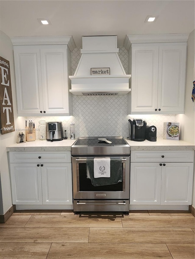 kitchen featuring light wood-type flooring, electric stove, custom exhaust hood, and white cabinets