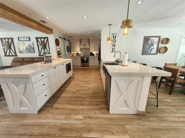 kitchen with wood finish floors, appliances with stainless steel finishes, a sink, a kitchen breakfast bar, and custom exhaust hood