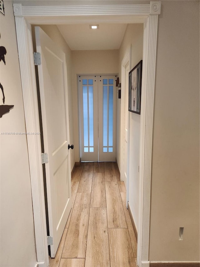 corridor with light wood-type flooring, baseboards, and french doors