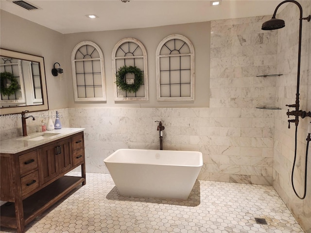 bathroom with visible vents, vanity, a freestanding tub, tile walls, and a tile shower
