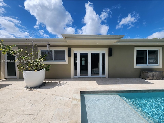 rear view of property with french doors, stucco siding, a patio area, and an outdoor pool