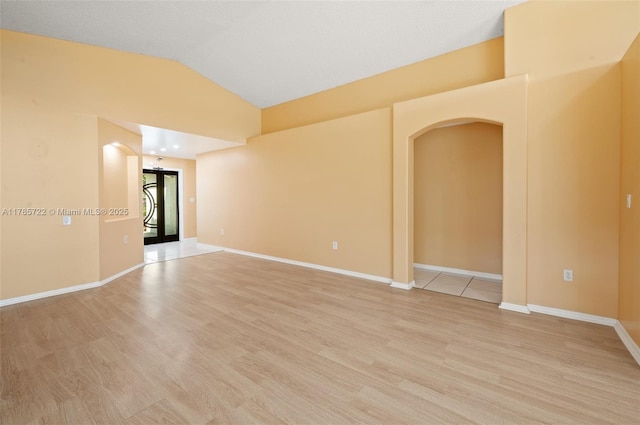 empty room featuring light wood-type flooring, arched walkways, baseboards, and vaulted ceiling