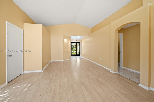 spare room with baseboards, arched walkways, light wood-style flooring, and vaulted ceiling