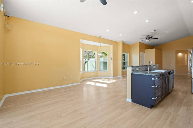 kitchen featuring a sink, a ceiling fan, baseboards, open floor plan, and light wood-type flooring
