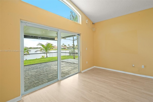 empty room with baseboards, light wood-type flooring, a textured ceiling, a water view, and vaulted ceiling