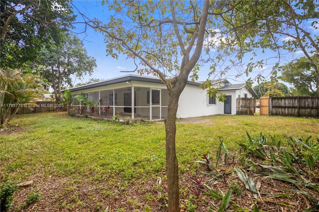 rear view of property with a lawn, a fenced backyard, stucco siding, and a sunroom