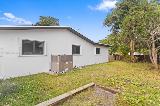 view of home's exterior with a garden, central AC, fence, stucco siding, and a yard