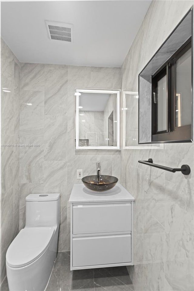 bathroom with vanity, toilet, marble finish floor, tile walls, and visible vents