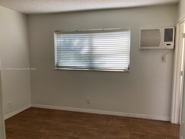 empty room featuring a wall mounted air conditioner, wood tiled floors, baseboards, and a textured ceiling