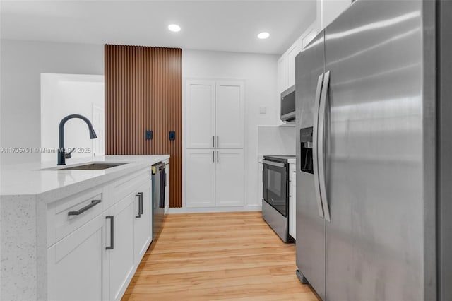 kitchen featuring appliances with stainless steel finishes, light stone counters, a sink, light wood-style flooring, and white cabinetry