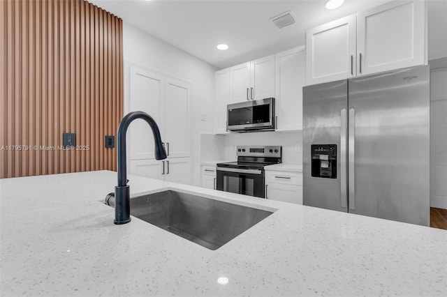 kitchen with appliances with stainless steel finishes, light stone counters, a sink, white cabinetry, and visible vents