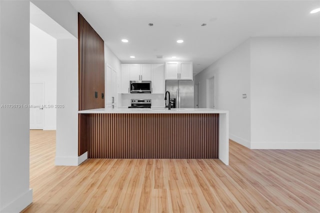 kitchen with baseboards, white cabinets, stainless steel appliances, and light wood finished floors