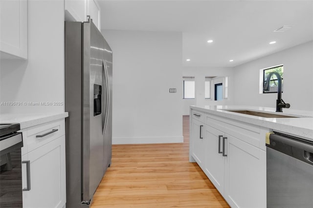 kitchen with a sink, stainless steel appliances, light wood finished floors, and white cabinetry